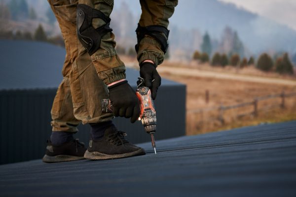 Male builder installing black corrugated iron sheet used as facade of future cottage. Man worker building wooden frame house. Carpentry and construction concept.