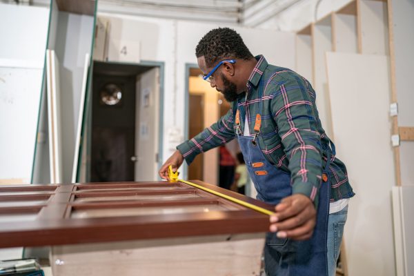 Manual worker using sander while working on a wood in carpentry workshop.