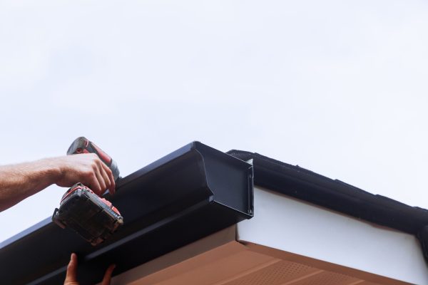 Worker installing rain gutter on roof is mounting downpipe